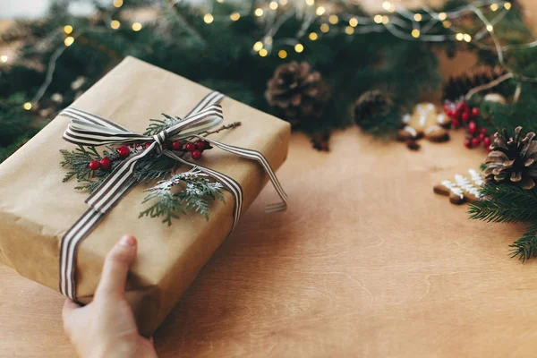 Рука тримає стильний сільський різдвяний подарунок і соснові гілки, co — стокове фото