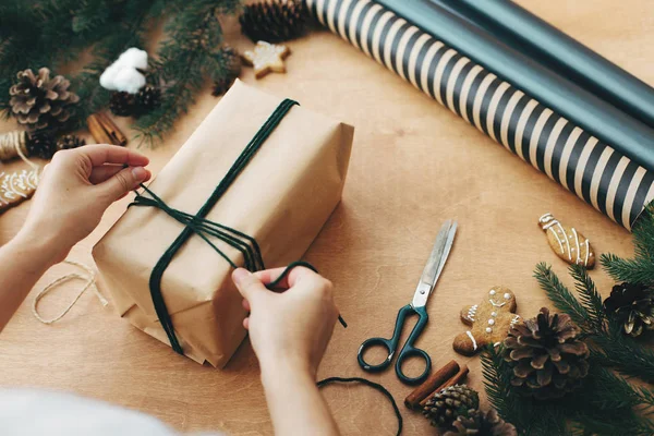 Manos que envuelven el regalo rústico de Navidad, atando el cordel verde, y el perno —  Fotos de Stock