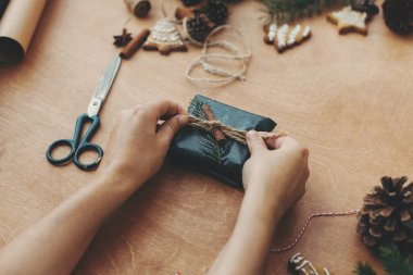 Noel hediyesini şık siyah kağıt ve çam ağacıyla saran eller.