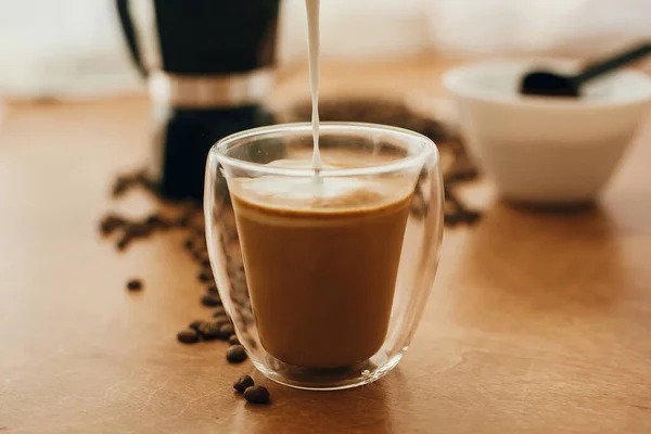 Verser le lait dans le café dans une tasse en verre sur fond de c torréfié — Photo