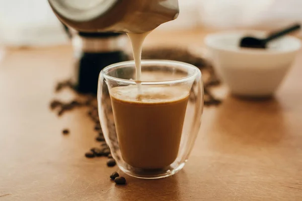 Pouring milk into coffee in glass cup on background of roasted c — Stock Photo, Image