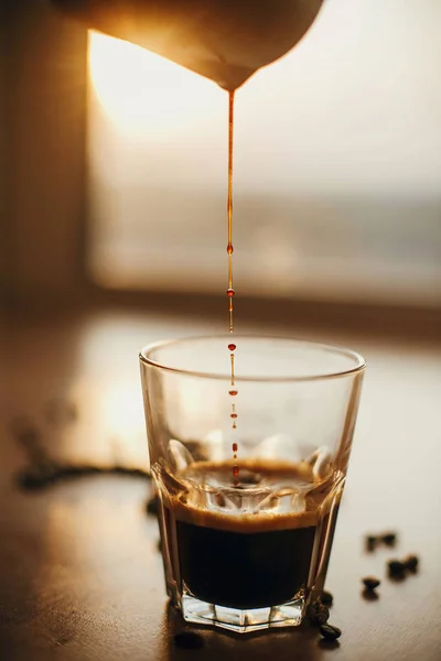 Pouring hot espresso in glass cup in warm light on background of — 스톡 사진
