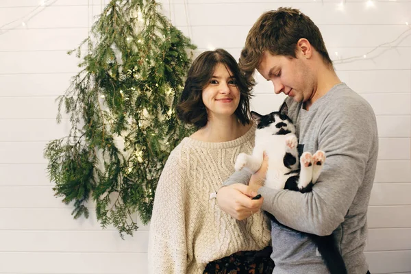 Happy hipster couple holding cat and having fun at christmas tre — Stock Photo, Image