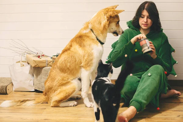 Happy girl in festive pajamas feeding dog and cat with canned fo — Stock Photo, Image