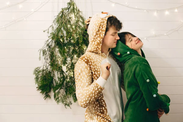 Happy couple in festive pajamas hugging at christmas tree lights — Stock Photo, Image