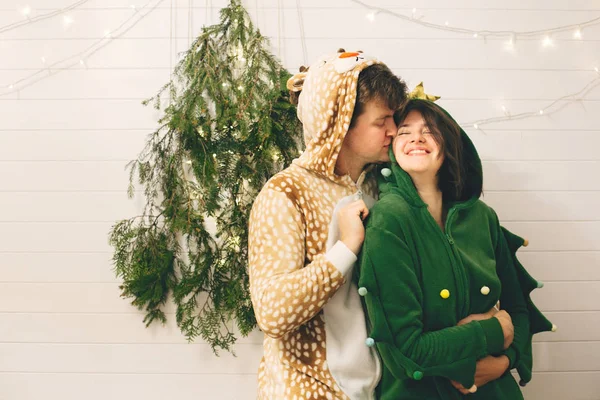 Happy couple in festive pajamas kissing at christmas tree lights — Stock Photo, Image