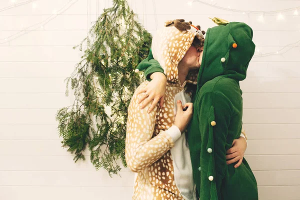 Happy couple in festive pajamas kissing at christmas tree lights — Stock Photo, Image