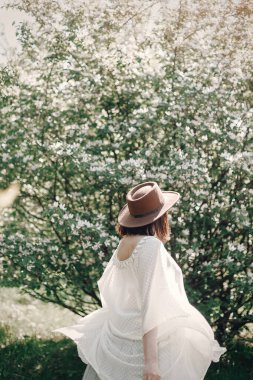 Şapkalı mutlu boho kadın beyaz blo yakınlarında güneşli ışıkta eğleniyor.