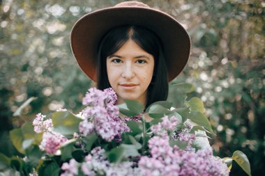 Şapkalı güzel bir kadının şehvetli portresi. Elinde leylak fl var.