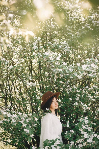 Stylowe boho kobieta w kapelusz pozowanie w kwitnące drzewo z biały flo — Zdjęcie stockowe