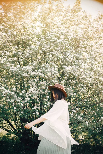 Feliz boho mujer en sombrero divirtiéndose en la luz soleada cerca de blo blanco —  Fotos de Stock