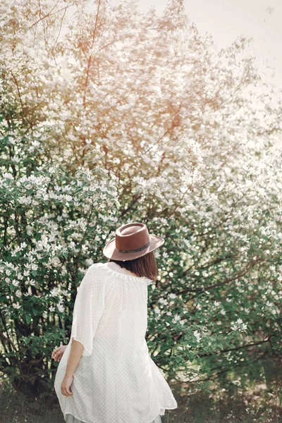 Boho feliz mulher no chapéu se divertindo na luz ensolarada perto de blo branco — Fotografia de Stock