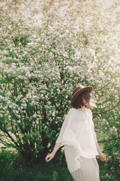 Boldog boho nő kalapban táncol napfényes fényben közel virágzó tre — Stock Fotó