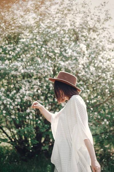 Feliz boho mujer en sombrero bailando en la luz soleada cerca de la floración tre — Foto de Stock
