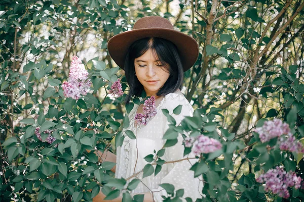 帽子のスタイリッシュなboho女性でポーズでライラック花で日当たりの良い春 — ストック写真