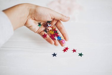 Hand holding colorful stars confetti or glitter on white backgro clipart