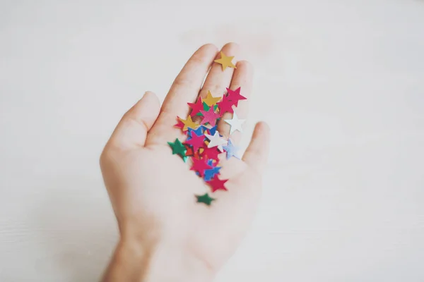 Mano sosteniendo estrellas coloridas confeti o purpurina sobre fondo blanco — Foto de Stock