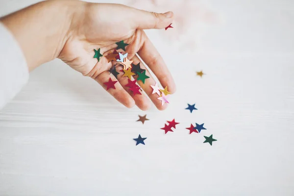 Mano sosteniendo coloridas estrellas brillantes decoraciones en el respaldo blanco — Foto de Stock