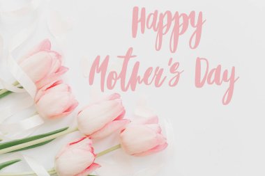 Anneler Günün kutlu olsun. Mutlu anneler günü mesajı ve beyaz arka planda pembe laleler. Yumuşak bir imaj. Çiçek tebrik kartı. Anneler Günün kutlu olsun. El yazısıyla yazılmış harfler