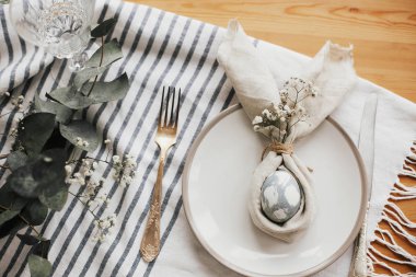 Paskalya masa süslemeleri. Paskalya kahvaltısı sofrasında yumurta ve paskalya tavşanı peçetesi. Modern doğal boyalı mavi yumurta peçetede tavşan kulağı, tabakta çiçekler ve klasik çatal bıçak takımı..