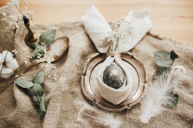 Kırsal Paskalya masa dekorasyonları. Paskalya kahvaltısı sofrasında yumurta ve paskalya tavşanı peçetesi. Tavşan kulaklı peçete üzerine modern doğal boyalı gri yumurta, klasik tabakta çiçekler..