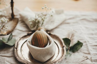 Kırsal Paskalya masa dekorasyonları. Paskalya kahvaltısı sofrasında yumurta ve paskalya tavşanı peçetesi. Tavşan kulaklı peçete üzerine modern doğal boyanmış yeşil yumurta, klasik tabakta çiçekler..