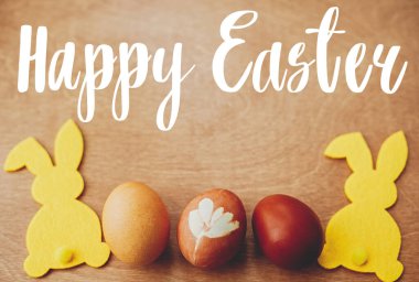 Mutlu Paskalya metinleri. Paskalya tebrik kartı. Şık paskalya yumurtaları ve kırsal ahşap masa üzerinde sarı tavşancık. Doğal boyanmış paskalya yumurtaları ve tavşan dekoru. Tatil kartı.
