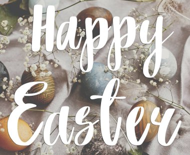 Mutlu Paskalya metinleri. Paskalya tebrik kartı. Kırsal masa üzerindeki paskalya yumurtaları düzleşmişti. Doğal renklerle boyanmış paskalya yumurtaları ilkbahar beyaz çiçekleri ve kırsal tekstil tüyleri.