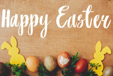 Mutlu Paskalya metinleri. Paskalya tebrik kartı. Şık paskalya yumurtaları, sarı tavşancık, kırsal ahşap masa üzerinde bahar çiçekleri. Doğal boyalı Paskalya yumurtası ve tavşan. Tatil kartı