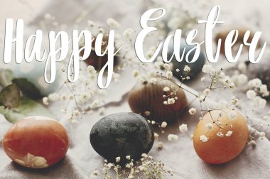 Mutlu Paskalya metinleri. Paskalya tebrik kartı. Kırsal masa üzerindeki paskalya yumurtaları düzleşmişti. Doğal renklerle boyanmış paskalya yumurtaları ilkbahar beyaz çiçekleri ve kırsal tekstil tüyleri.