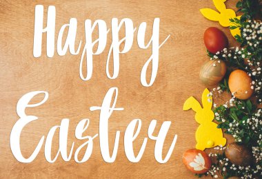 Mutlu Paskalya metinleri. Paskalya tebrik kartı. Şık paskalya yumurtaları, sarı tavşancık, kırsal ahşap masa üzerinde bahar çiçekleri. Doğal boyalı Paskalya yumurtası ve tavşan. Tatil kartı