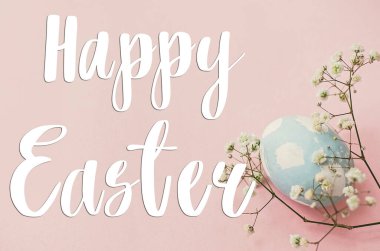 Mutlu Paskalya metinleri. Paskalya tebrik kartı. Pembe kağıt üzerinde paskalya yumurtası ve bahar çiçekleri. Modern doğal boyanmış mavi paskalya yumurtası. Tatil kartı