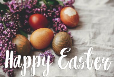 Mutlu Paskalya metinleri. Paskalya tebrik kartı. Kırsal keten kumaş ve mor leylak çiçekli modern renkli Paskalya yumurtaları. Kırsal yaşam. Doğal boyalı paskalya yumurtaları. Tatil kartı