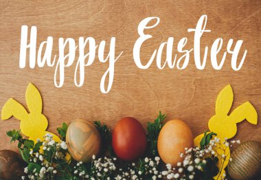 Mutlu Paskalya metinleri. Paskalya tebrik kartı. Şık paskalya yumurtaları, sarı tavşancık, kırsal ahşap masa üzerinde bahar çiçekleri. Doğal boyalı Paskalya yumurtası ve tavşan. Tatil kartı
