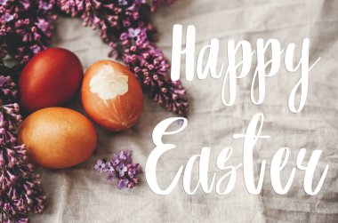 Mutlu Paskalya metinleri. Paskalya tebrik kartı. Kırsal keten kumaş ve mor leylak çiçekli modern renkli Paskalya yumurtaları. Kırsal yaşam. Doğal boyalı paskalya yumurtaları. Tatil kartı