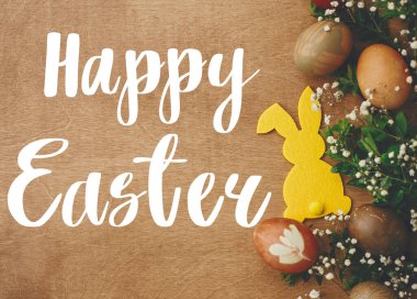 Mutlu Paskalya metinleri. Paskalya tebrik kartı. Şık paskalya yumurtaları, sarı tavşancık, kırsal ahşap masa üzerinde bahar çiçekleri. Doğal boyalı Paskalya yumurtası ve tavşan. Tatil kartı