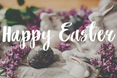 Mutlu Paskalya metinleri. Paskalya tebrik kartı. Modern Paskalya yumurtaları, beyaz tavşanlar ve keten kumaşlı leylak çiçekleri. Doğal boyanmış paskalya yumurtaları ve bahar çiçekleri. Tatil kartı