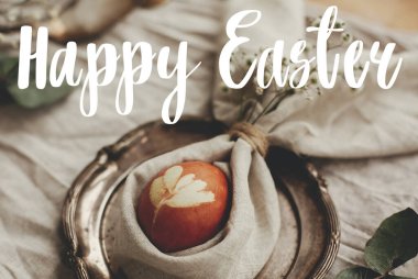 Mutlu Paskalya metinleri. Paskalya tebrik mektupları. Tavşan kulaklı peçeteli Paskalya yumurtası ve kırsal masada çiçekler. Modern kırmızı yumurta. Tatil masası süslemeleri. Tebrik kartı