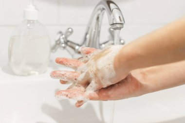 Ellerini yıka! Parmaklarını ovuşturmak, beyaz banyoda akan suyun arka planında antibakteriyel sabunla ellerini yıkamak. Koronavirüsü önleme. Temizleme ve dezenfekte etme