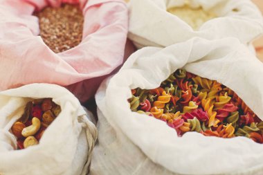 Sıfır atık. Tekrar kullanılabilir tekstil poşetlerindeki yiyecekler ahşap masada. Mısır gevreği, makarna, un, poşetlerdeki tahıllar, plastik poşetlerden ücretsiz teslimat. Plastiği yasakla