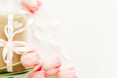 Beyaz arka planda, kurdeleli pembe laleler ve hediye kutusu, düz. Zarif bir imaj. Mesaj için yeri olan tebrik kartı. Sevgililer günün kutlu olsun. Düğün ya da sevgililer günü modeli. Mutlu kadınlar günü.