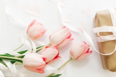 Merhaba bahar. Kurdeleli pembe laleler ve beyaz arka planda hediye kutusu. Bahar çiçeklerinin şık, yumuşak bir görüntüsü. Mutlu kadınlar günü. Tebrik kartı modeli. Anneler Günün kutlu olsun..