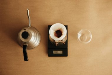 Düz kahve döşemesi. Çelik çaydanlık, filtreli cam matara ve kahverengi arka planda cam bardak. Alternatif aromatik kahve, v60
