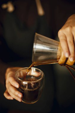 Siyah üniformalı profesyonel bayan barista damlatan kahve yapıyor. Cam şişeden taze aromatik kahveyi dolduran kişi ellerini kapasın. Alternatif kahve, v60.