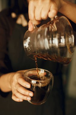 Bardaktaki cam çaydanlıktan taze aromatik kahve dolduran kişi. Alternatif kahve, v60. Siyah üniformalı profesyonel barista damlatan kahve yapıyor.