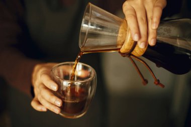 Siyah üniformalı profesyonel bayan barista damlatan kahve yapıyor. Cam şişeden taze aromatik kahveyi dolduran kişi ellerini kapasın. Alternatif kahve, v60.