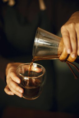 Cam şişeden taze aromatik kahveyi dolduran kişi ellerini kapasın. Alternatif kahve, v60. Siyah üniformalı profesyonel bayan barista damlatan kahve yapıyor..