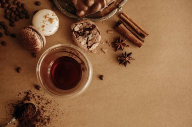 Kahve karamsarlığı. Taze kahve ve kızarmış fasulye, kaşık üzerinde öğütülmüş kahve, makaron, çikolata, kahverengi arka planda tarçın. Üst Manzara. Görüntü stili