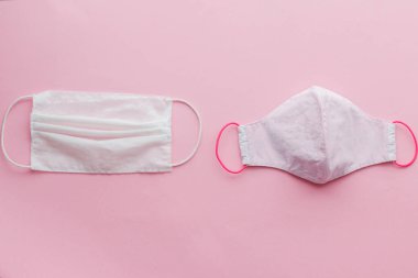 Yeniden kullanılabilir yüz maskesi ve pembe arka planda tek kullanımlık tıbbi maske. Coronavirüs salgını sırasında sıfır atık kavramı. Tek kullanımlık maske ve el yapımı tekstil maskesi
