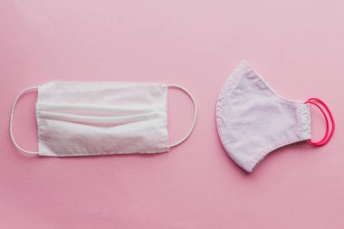 Yeniden kullanılabilir yüz maskesi ve pembe arka planda tek kullanımlık tıbbi maske. Coronavirüs salgını sırasında sıfır atık kavramı. Tek kullanımlık maske ve el yapımı tekstil maskesi